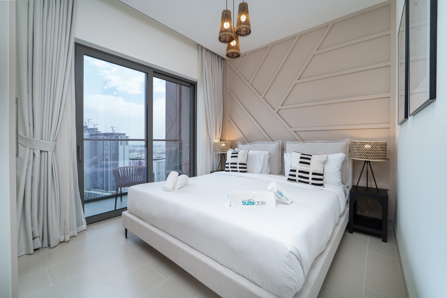 Modern luxury bedroom with city skyline view through floor-to-ceiling windows, white bedding, and contemporary pendant lighting