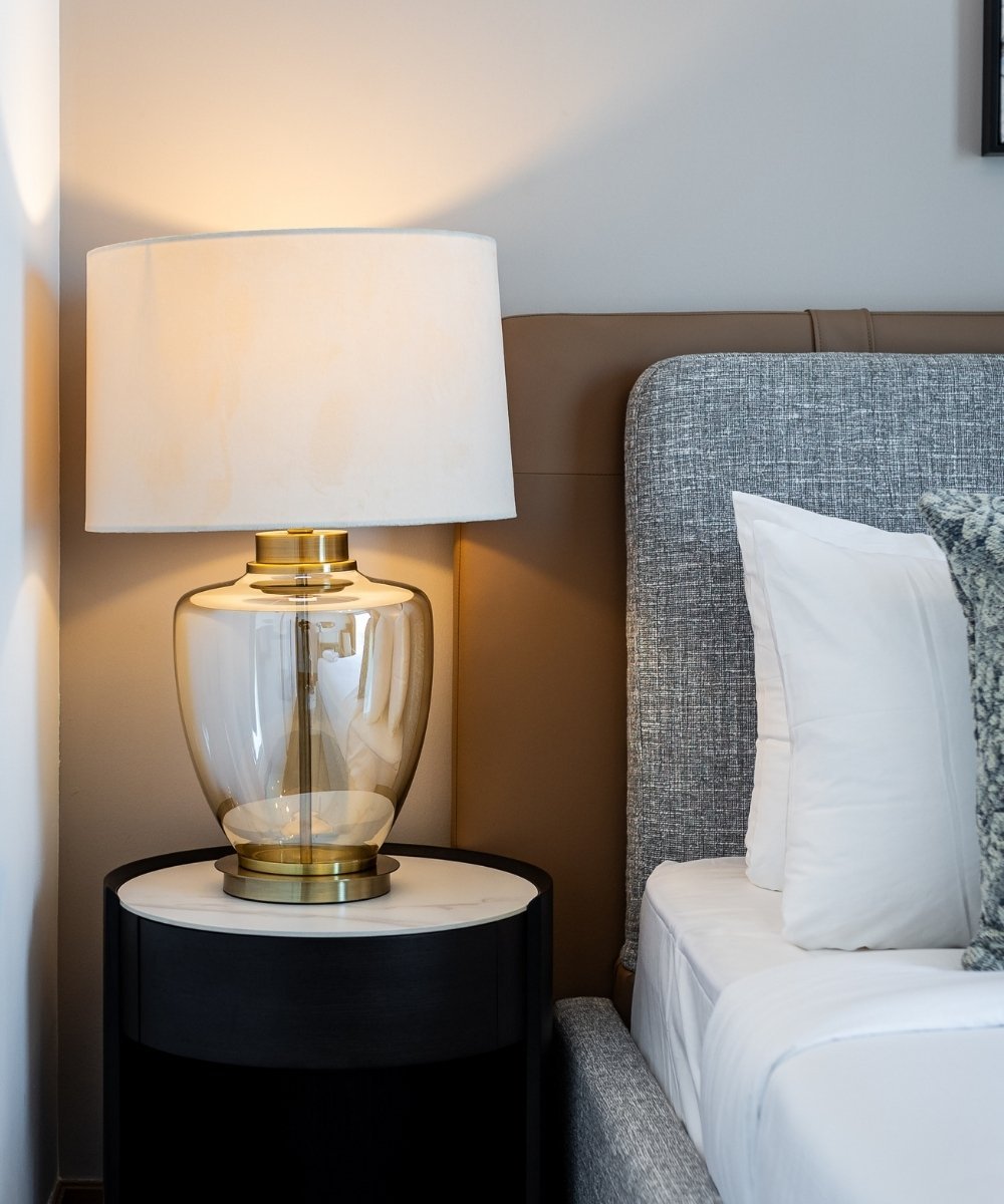 Clean and organized bedroom with elegant gold table lamp, white bedding, and modern bedside table